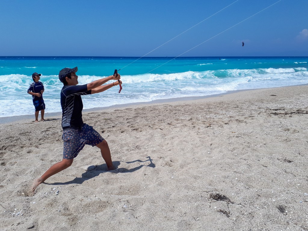 A teenager learning to kite on Agios Ioannis beach Lefkada with a trainer kite and the clear blue sea in the background