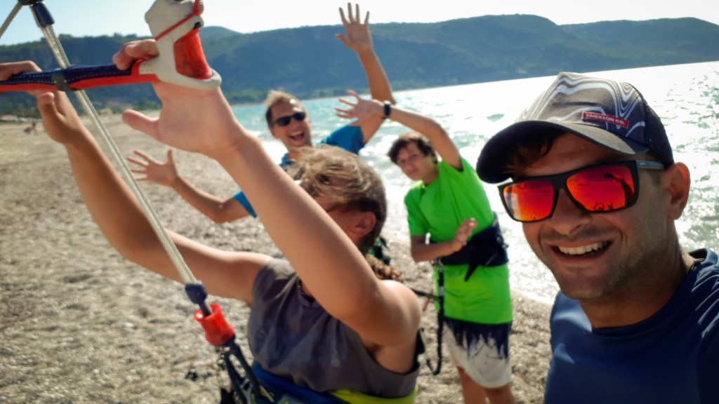 Four people with three of them smiling on the beach learning to control a kite for kitesurf