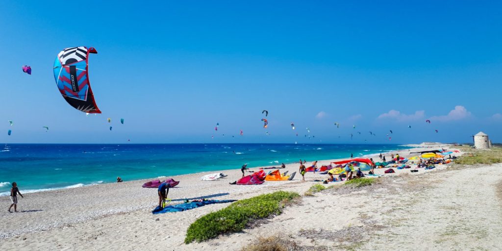 Agios Ioannis beach Lefkada with kites in the air and on the beach with kitesurfers and a windmill and clear blue sea and sky